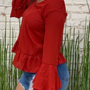 African American woman standing with one hand on face, looking to the side. Wearing orange long sleeve top.