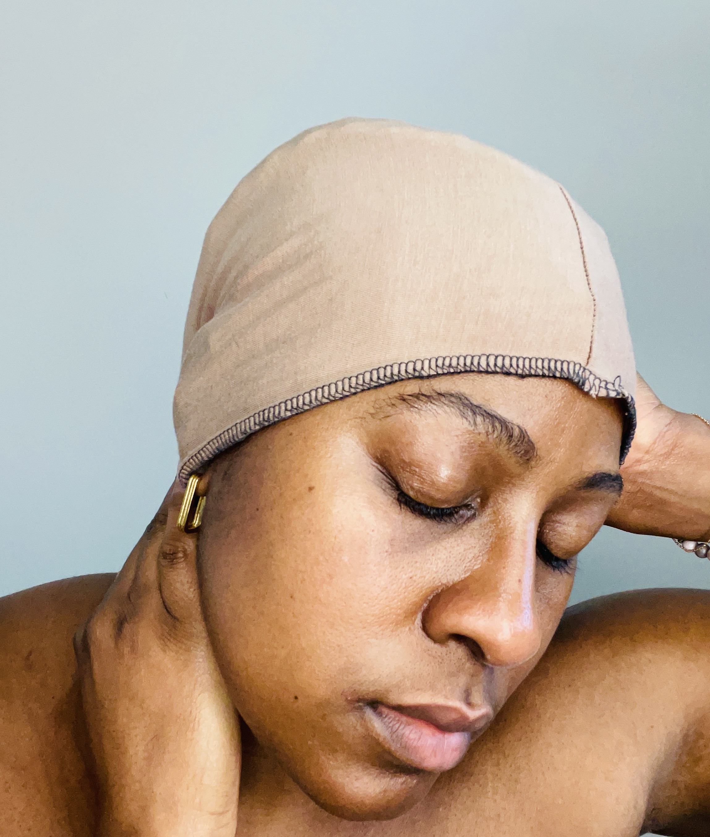 African American woman with eyes closed with head towards shoulder. Wearing tan fitted fabric on head.