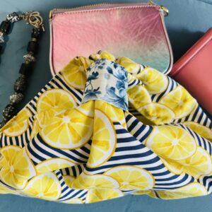 Arial view of lemon and strip patterned bag. With necklace on side along with pink wallet and pouch.